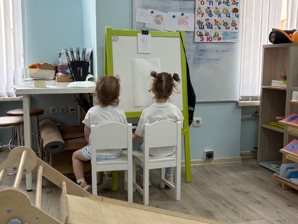 Две девочки рисуют у мольберта