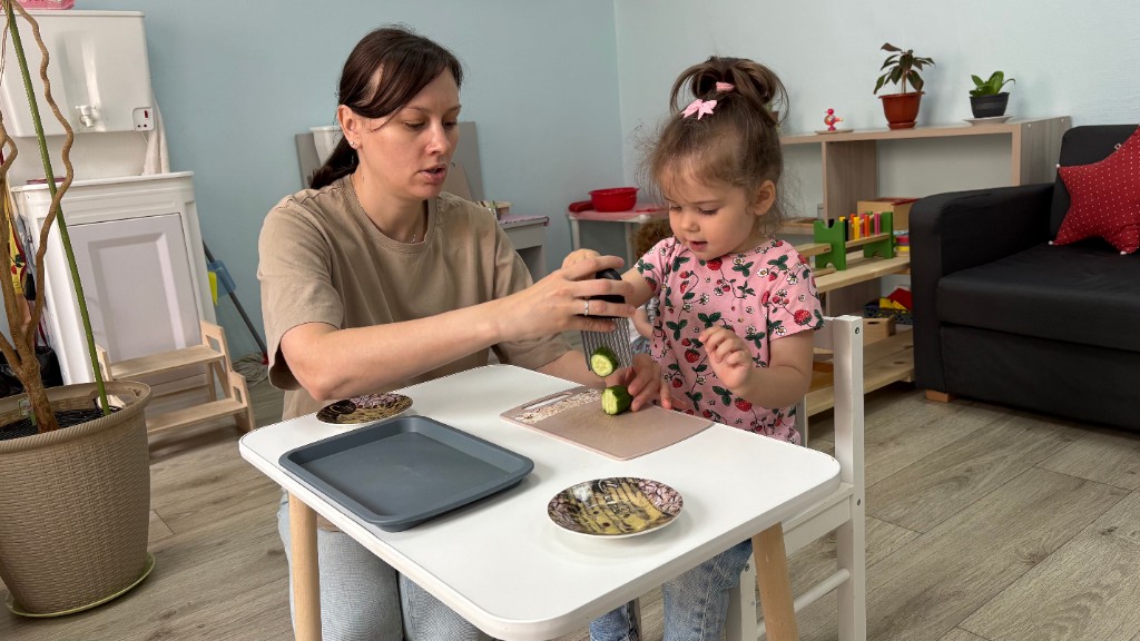 Педагог помогает ребёнку нарезать огурец